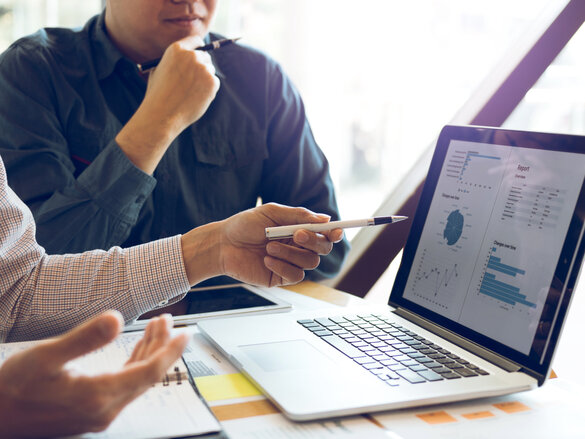 Two businessmen are together analyzing the financial data graph and pointing to the laptop computer screen.