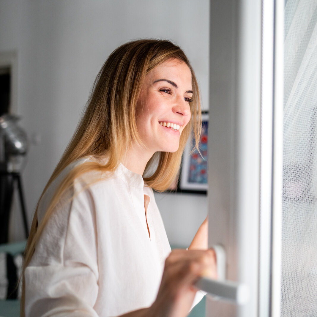 Frau öffnet Fenster und atmet frische Luft ein