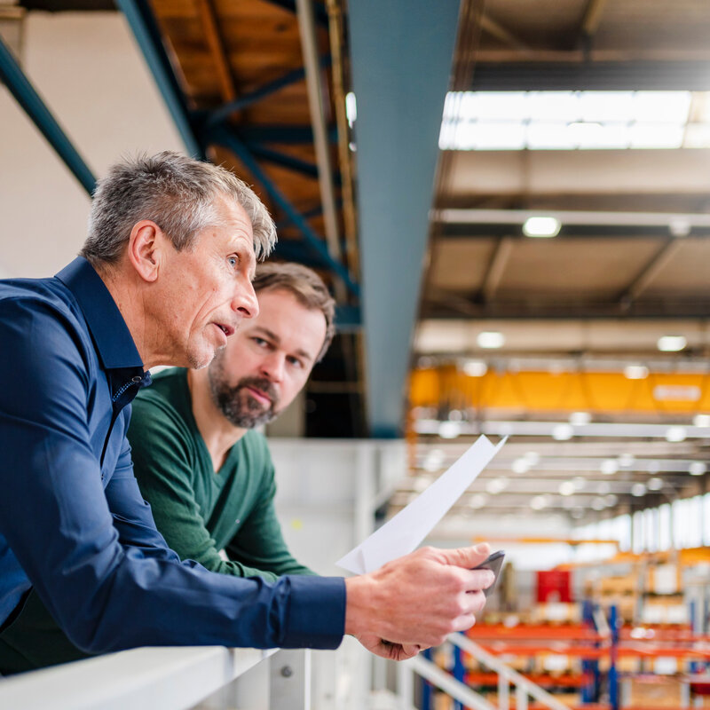 Two men standing in a hall, engaged in a discussion about plans for energy-efficient cooling solutions